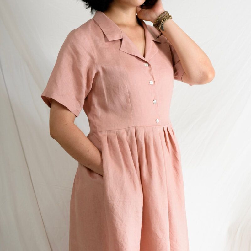Crafted from breathable 100% linen, this pastel pink dress features a relaxed fit with short sleeves, a soft pleated skirt, and delicate mother-of-pearl buttons. The natural texture of linen pairs beautifully with the structured collar, offering a timeless look inspired by effortless summer dressing.