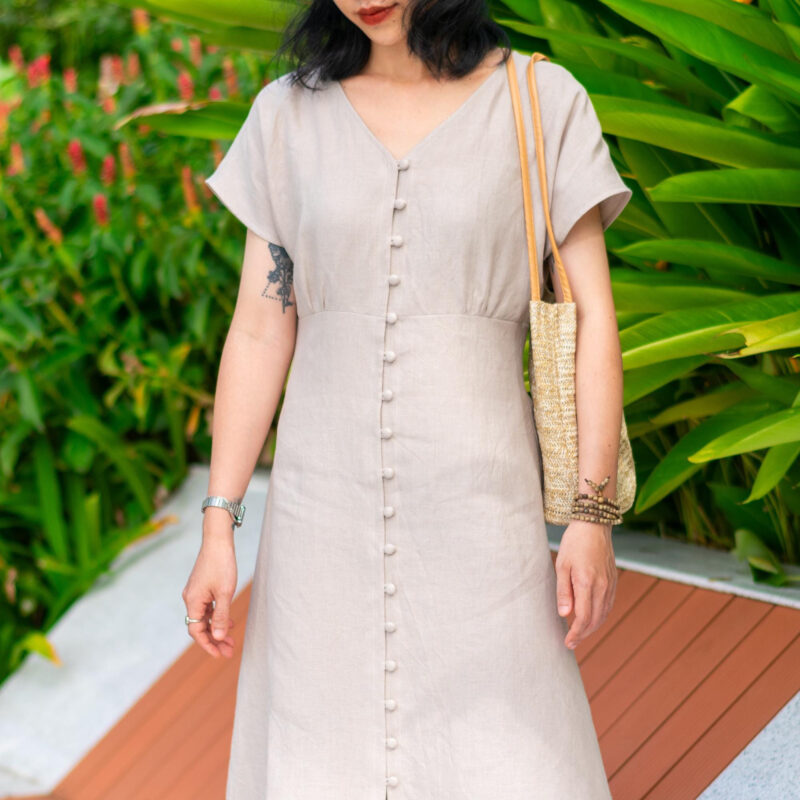 This light beige linen dress features a flattering V neckline and a full front row of fabric-covered buttons. Made from breathable 100% natural linen, it's perfect for warm weather and relaxed outdoor settings. The minimalist silhouette flows gracefully, making it ideal for garden strolls or weekend getaways.