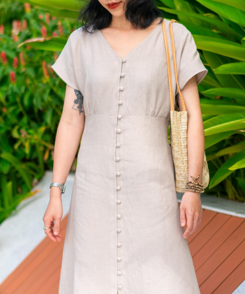 This light beige linen dress features a flattering V neckline and a full front row of fabric-covered buttons. Made from breathable 100% natural linen, it's perfect for warm weather and relaxed outdoor settings. The minimalist silhouette flows gracefully, making it ideal for garden strolls or weekend getaways.