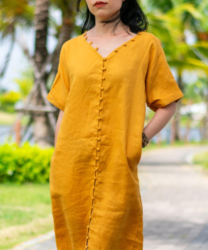 A mustard yellow linen dress with a soft V-neckline and handcrafted fabric-covered buttons running down the center. Made from breathable natural linen, the dress features a straight, relaxed silhouette and rolled short sleeves, ideal for summer outings or casual strolls. Inspired by tropical sunshine and slow living aesthetics.