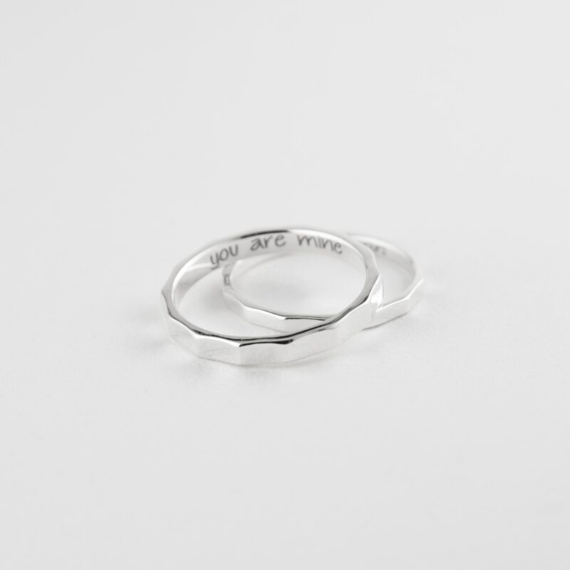 Flat-lay of two 925 sterling silver bamboo couple rings overlapping on white. Engravings "you are mine" and "I am yours" peek inside. Faceted texture highlights craftsmanship, perfect for a personalized love gift.