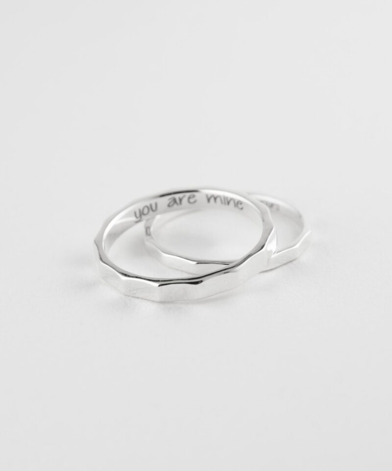 Flat-lay of two 925 sterling silver bamboo couple rings overlapping on white. Engravings "you are mine" and "I am yours" peek inside. Faceted texture highlights craftsmanship, perfect for a personalized love gift.