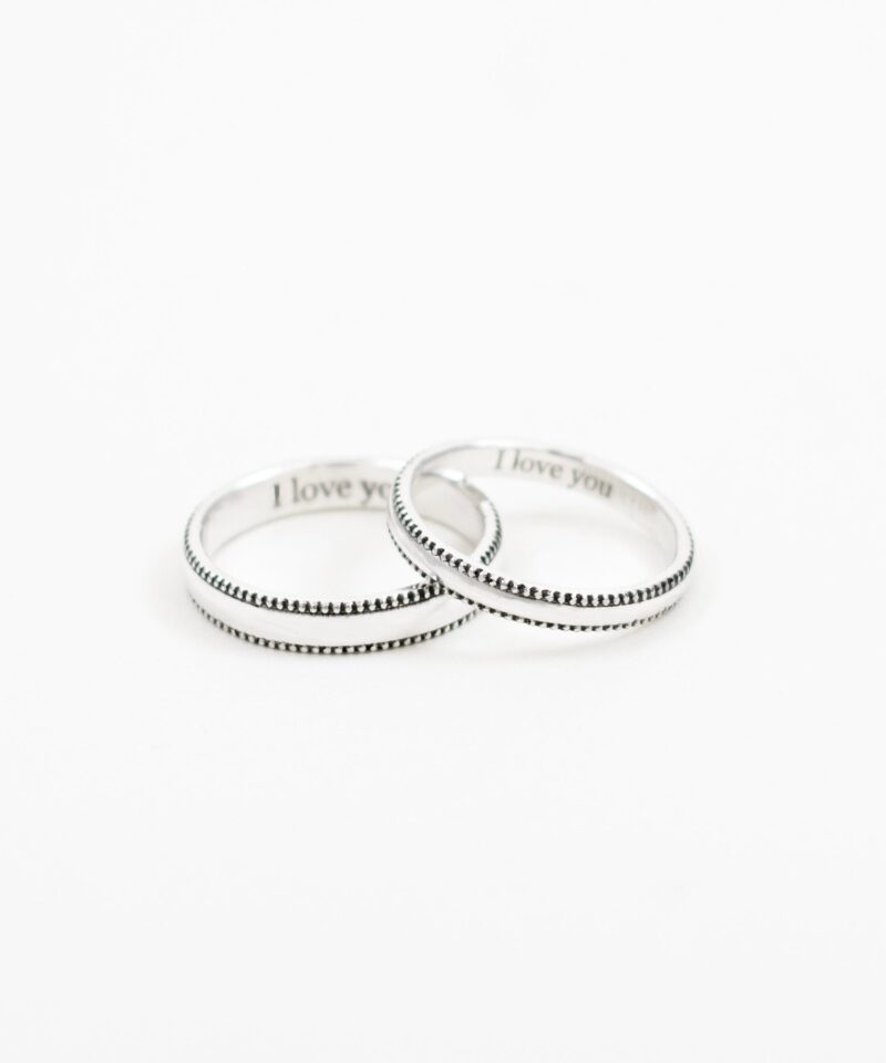 This close-up image showcases a pair of minimalist sterling silver couple rings, positioned at a gentle angle to highlight their delicate beaded edge design. The engraving 