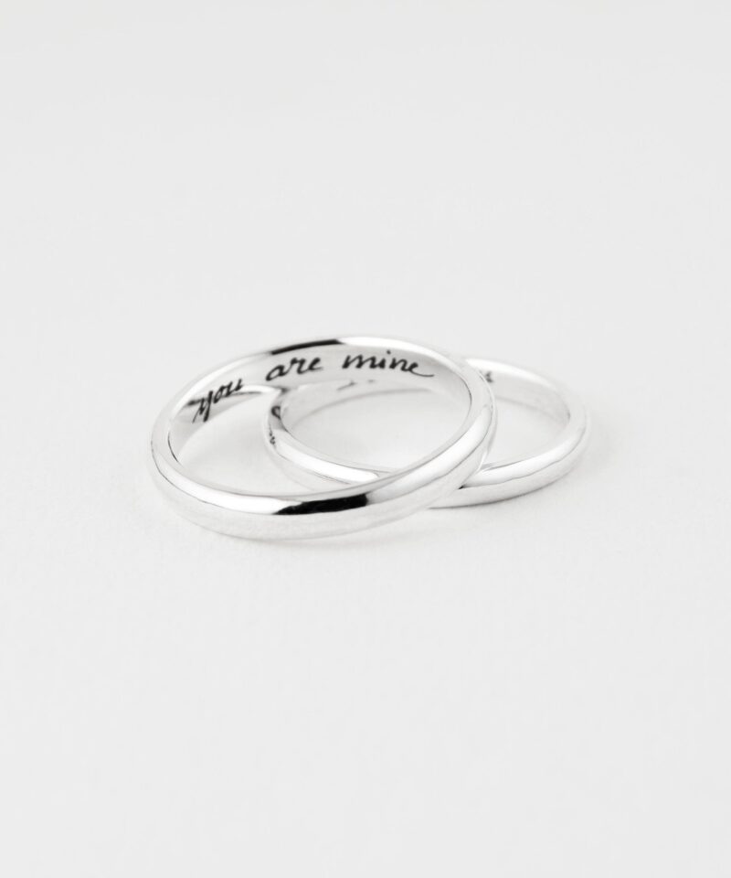 Close-up shot of two minimalist sterling silver couple rings elegantly interlocked on a white surface. One ring is engraved inside with the phrase 