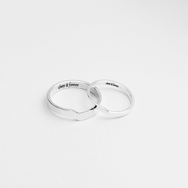 A pair of minimalist sterling silver couple rings photographed on a white background. Each ring features a subtle geometric notch that aligns perfectly when placed together, symbolizing deep connection and unity. The inner side of the rings is engraved with the phrase "always & forever," offering a heartfelt personalization. Their high-polished silver finish adds an elegant, modern touch, ideal for matching promise rings or anniversary gifts.