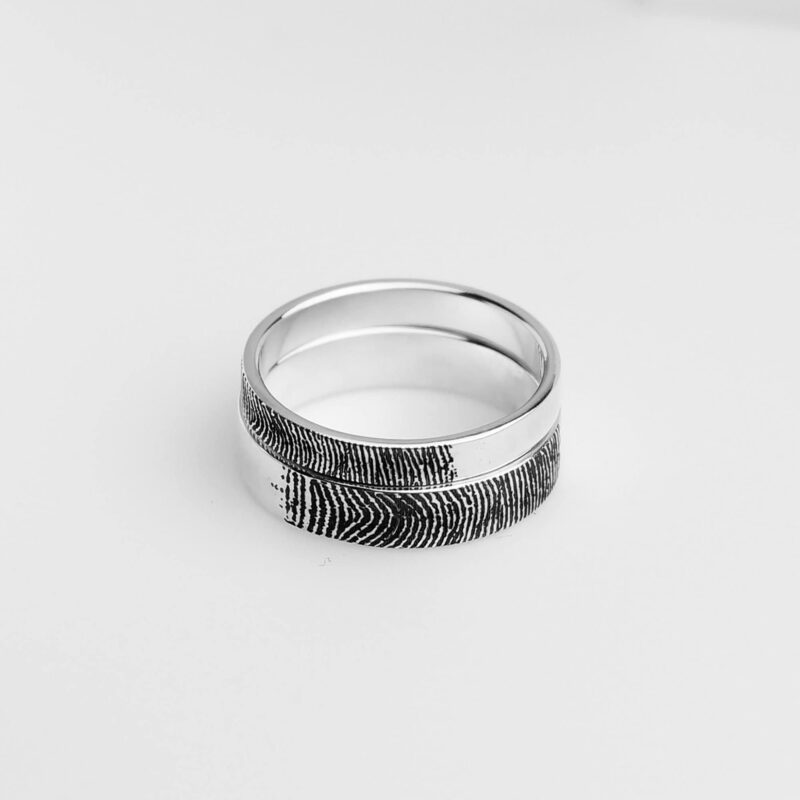 A close-up of a 925 sterling silver couple ring set showcasing a beautifully aligned fingerprint engraving across both rings. The black oxidized texture creates a striking contrast on the polished silver band, symbolizing a unique and personal connection between two lovers. The minimalist design with meaningful detail makes these rings a timeless representation of shared identity and love.