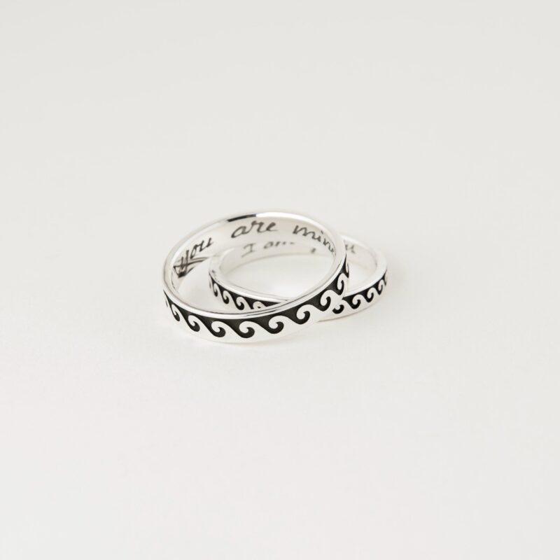Two sterling silver couple rings with Greek wave patterns, stacked slightly to reveal inside engravings “You are mine” and “I am yours” in handwritten style, photographed on white background to highlight the clean polish and symbolic design.