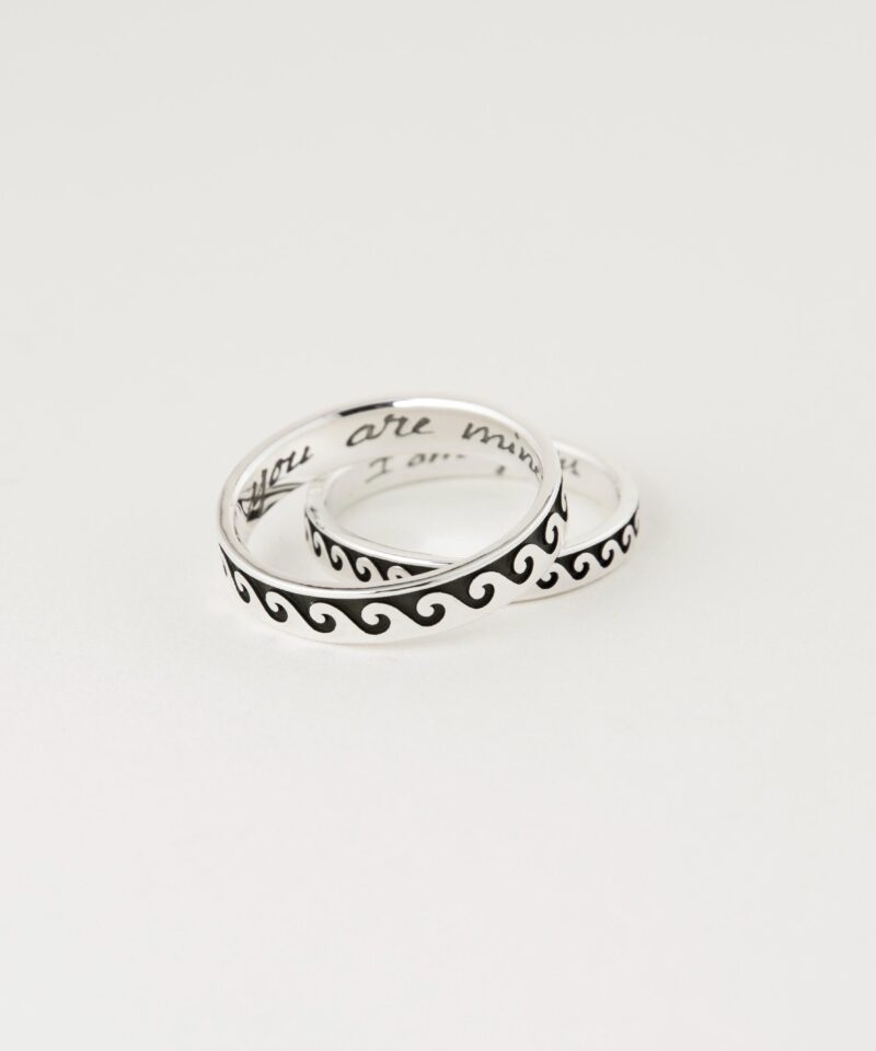 Two sterling silver couple rings with Greek wave patterns, stacked slightly to reveal inside engravings “You are mine” and “I am yours” in handwritten style, photographed on white background to highlight the clean polish and symbolic design.