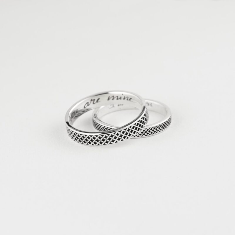 Artistic product shot of a handcrafted sterling silver couple ring set, resting elegantly on a white background. The rings feature a repeating oxidized lattice design and engraved messages inside, “you are mine” and “I am yours.” The polished finish and handcrafted texture make them a heartfelt gift for couples celebrating connection, loyalty, and personalization.