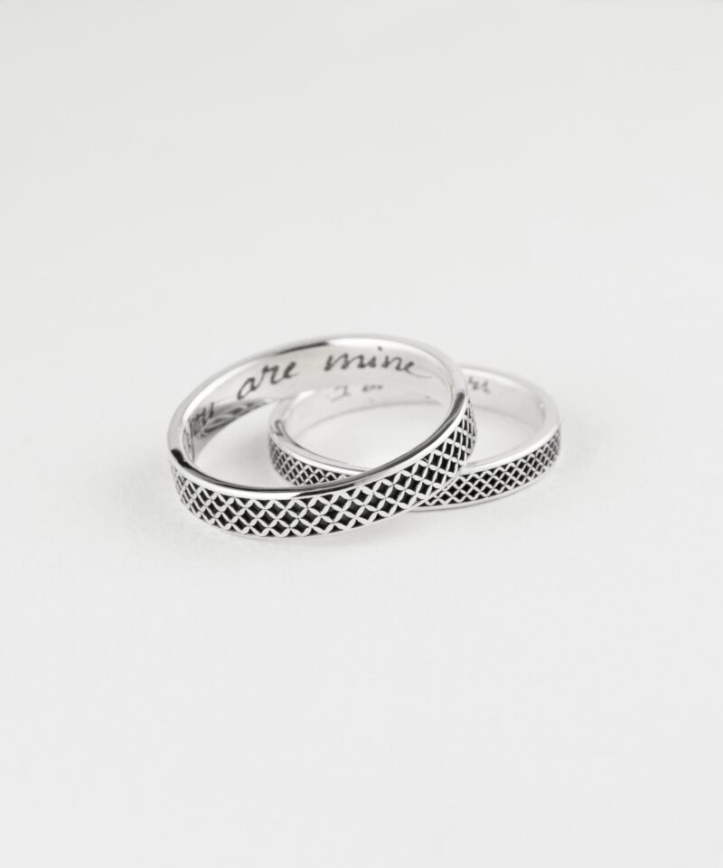 Artistic product shot of a handcrafted sterling silver couple ring set, resting elegantly on a white background. The rings feature a repeating oxidized lattice design and engraved messages inside, “you are mine” and “I am yours.” The polished finish and handcrafted texture make them a heartfelt gift for couples celebrating connection, loyalty, and personalization.