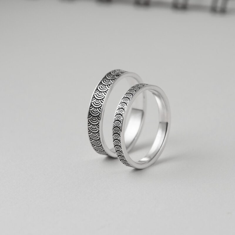 Artistic studio shot of two silver rings propped vertically, revealing both outer wave motif and inner smooth finish. The layered look adds dimension and showcases craftsmanship, ideal for highlighting the contrast between texture and polish. This timeless Japanese pattern evokes flowing movement and shared journeys—suitable for anniversary or vow rings.