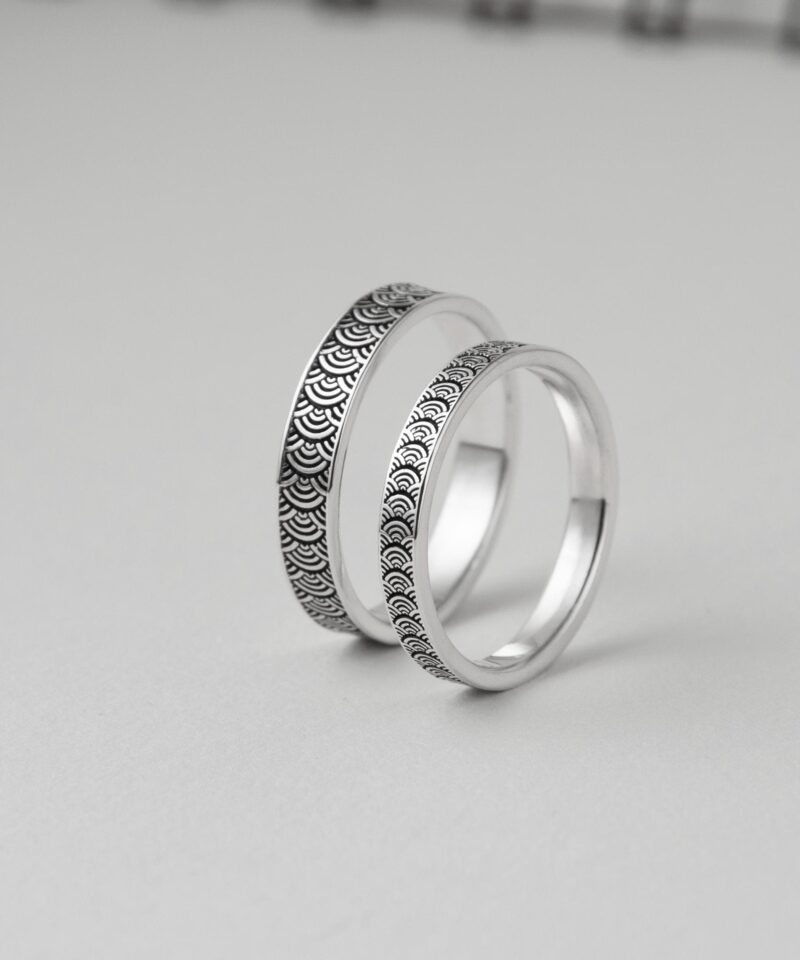 Artistic studio shot of two silver rings propped vertically, revealing both outer wave motif and inner smooth finish. The layered look adds dimension and showcases craftsmanship, ideal for highlighting the contrast between texture and polish. This timeless Japanese pattern evokes flowing movement and shared journeys—suitable for anniversary or vow rings.