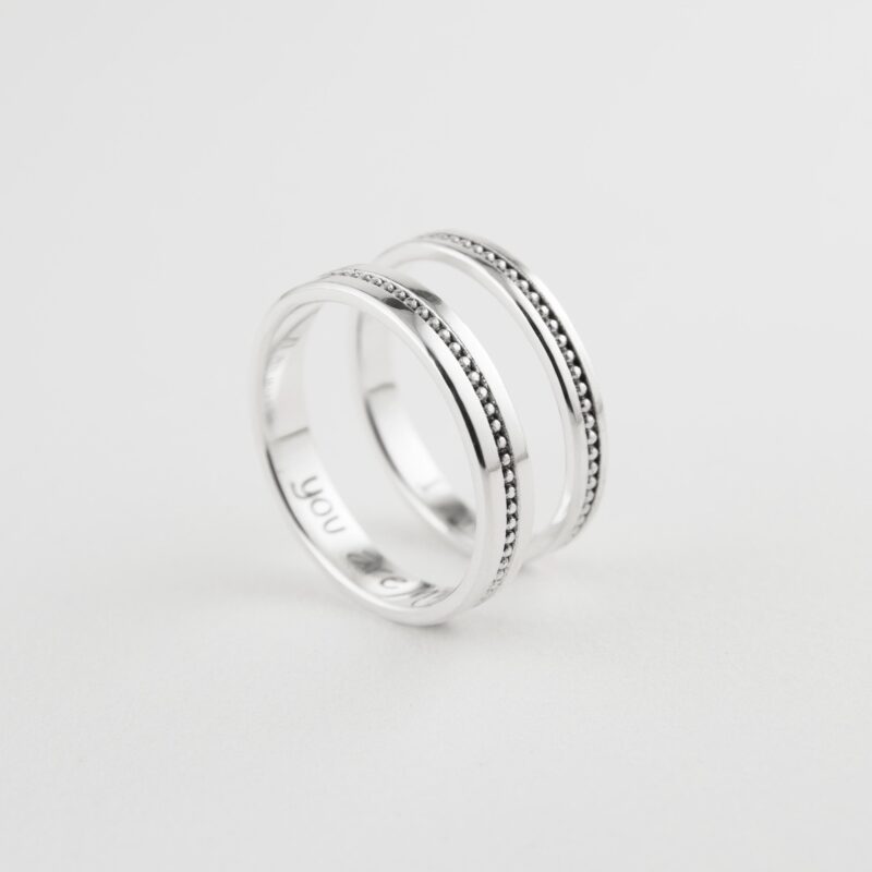 A lovely arrangement of two matching sterling silver rings standing side by side on a white background. The milgrain beaded details shimmer subtly under soft lighting, highlighting the craftsmanship and delicate texture of each band. These rings celebrate love through minimalist elegance, ideal for meaningful everyday moments.