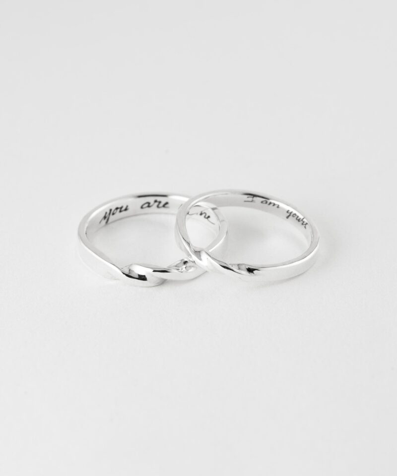 Silver Mobius Twist couple rings gently overlapped on a clean white surface. The soft sculptural twist at the center adds dynamic flow to the design, while engraved messages inside personalize each piece. A timeless jewelry set that speaks of commitment and harmony.
