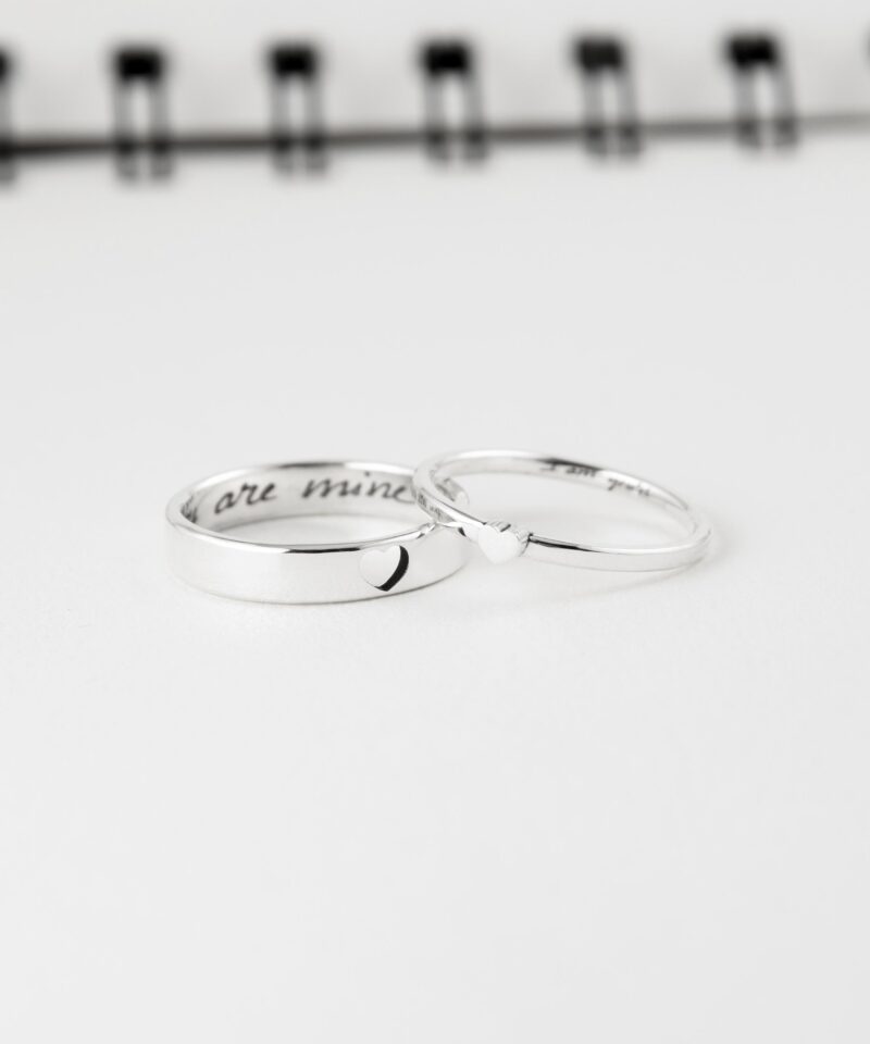 This close-up photo displays a pair of 925 sterling silver couple rings lying side by side. The men’s ring features a hollow heart, and the women’s ring has a raised heart that interlocks when placed together. Inside both rings are engraved messages in delicate script. These handcrafted rings symbolize unity and are perfect for gifting on anniversaries, weddings, or special occasions.