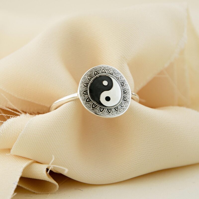 A sterling silver Yin Yang ring captured on soft cream fabric, with the iconic black and white symbol prominently centered inside a mandala-engraved frame. The textured fabric background adds a soft, luxurious aesthetic that complements the ring’s reflective surface and intricate design. Ideal for gifting, meditation, or self-expression, this piece blends philosophy and minimalism with handmade charm.