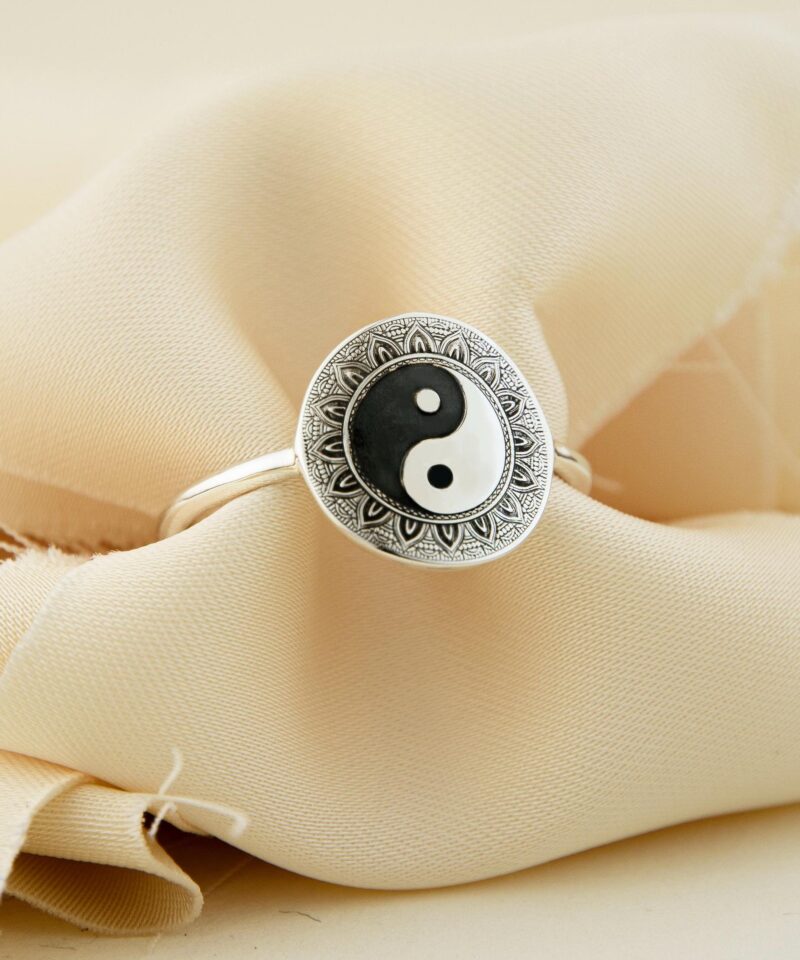 A sterling silver Yin Yang ring captured on soft cream fabric, with the iconic black and white symbol prominently centered inside a mandala-engraved frame. The textured fabric background adds a soft, luxurious aesthetic that complements the ring’s reflective surface and intricate design. Ideal for gifting, meditation, or self-expression, this piece blends philosophy and minimalism with handmade charm.