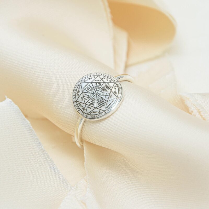 Handmade sterling silver Seven Archangels ring placed on cream-colored satin folds, highlighting the sacred seal engraving. The polished silver band and mystical design reflect a soft spiritual elegance.