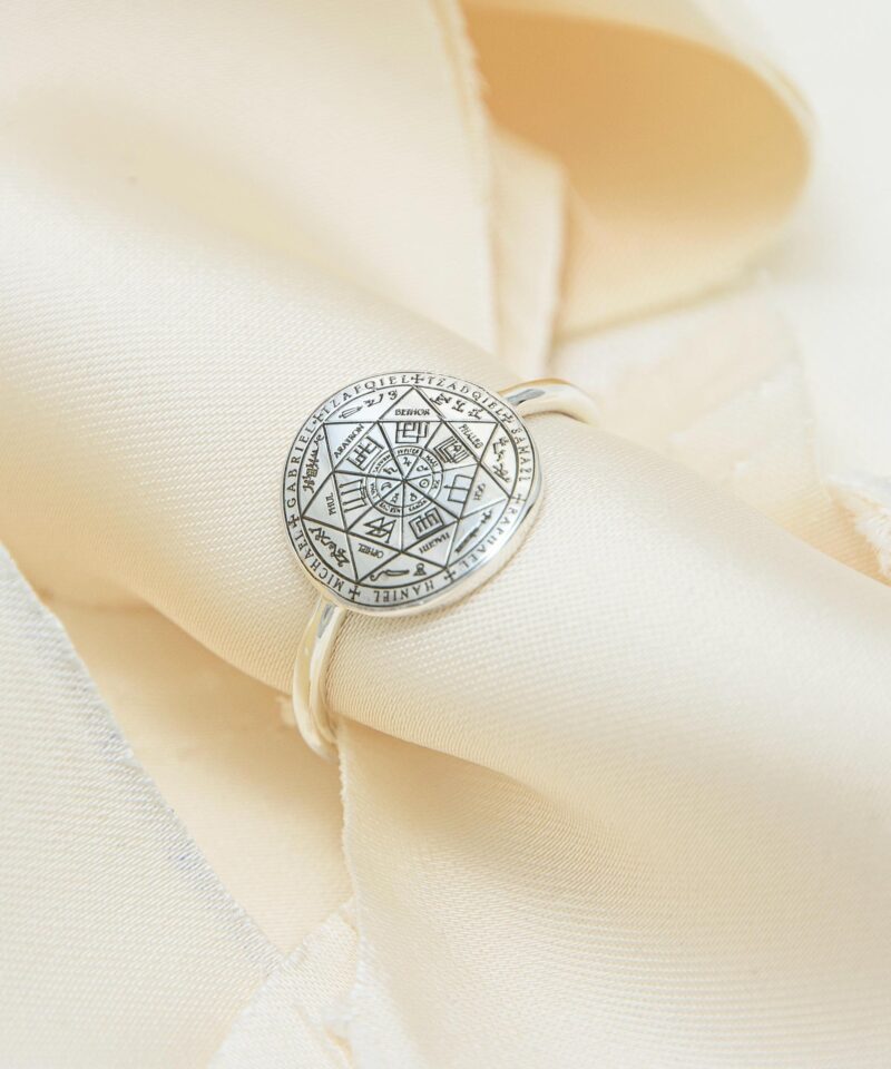Handmade sterling silver Seven Archangels ring placed on cream-colored satin folds, highlighting the sacred seal engraving. The polished silver band and mystical design reflect a soft spiritual elegance.