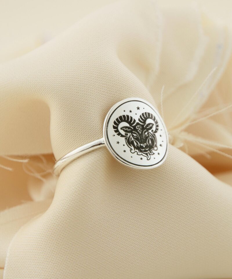 Close-up of the Aries zodiac silver ring, crafted from solid 925 sterling silver with a polished oval face engraved with a majestic ram and surrounding stars. Displayed on elegant cream-colored fabric, this astrology-inspired ring is ideal for personalized horoscope gifts or spiritual statement jewelry with symbolic meaning for Aries individuals.