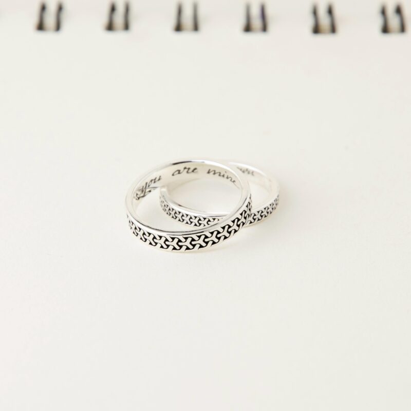 A close-up of two sterling silver couple rings featuring a Japanese geometric pattern. The rings are stacked together, highlighting the intricate oxidized texture and engraved inner band with “You are mine” and “I am yours”.