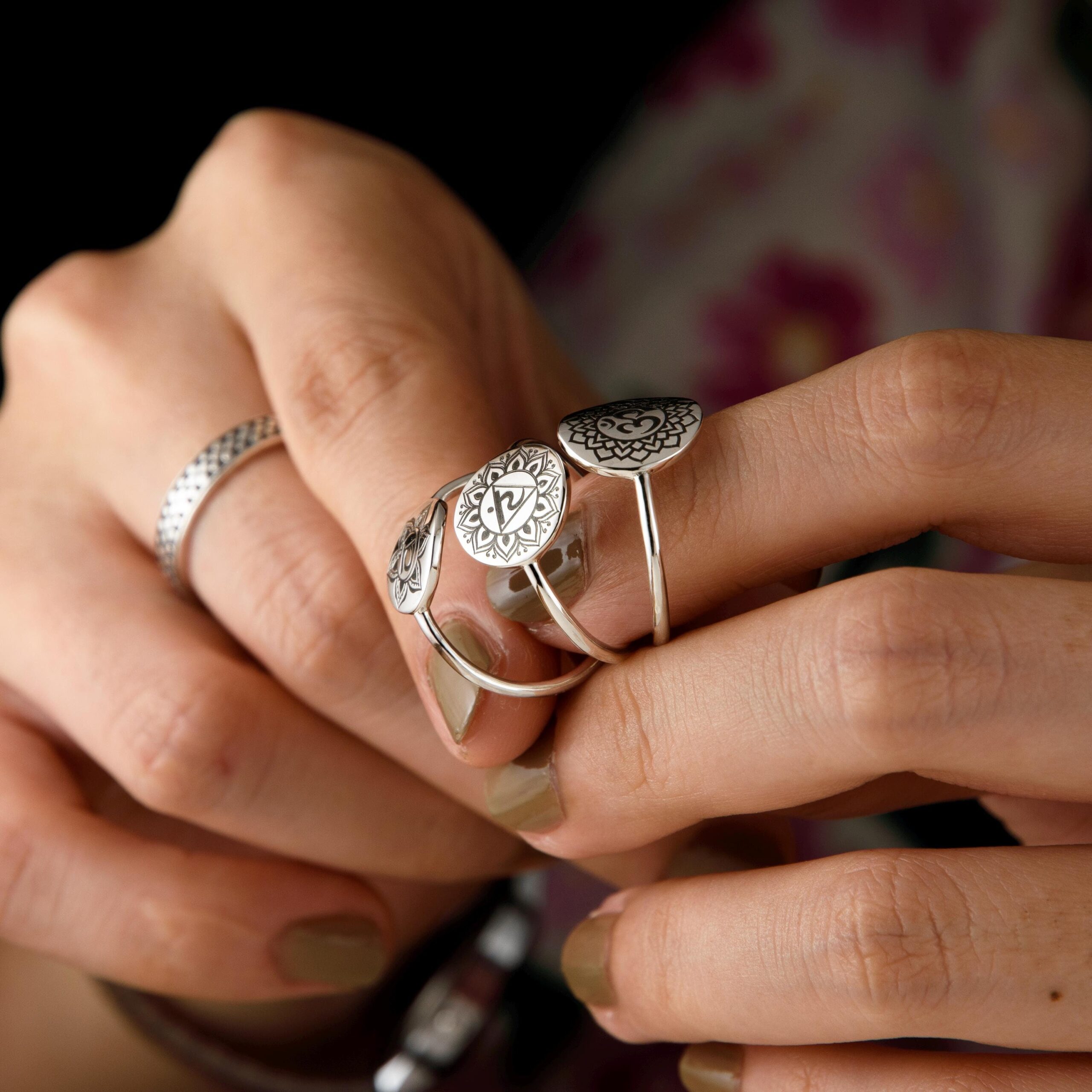 Close-up of a woman's hand wearing three chakra rings on adjacent fingers, each ring showcasing a different Sanskrit symbol engraved into sterling silver. The bold chakra icons — heart, throat, and crown — are encircled by finely detailed lotus petals. Ideal for meditation, reiki, or yoga practice, these rings bring grounding and balance with style. A perfect accessory for conscious souls.