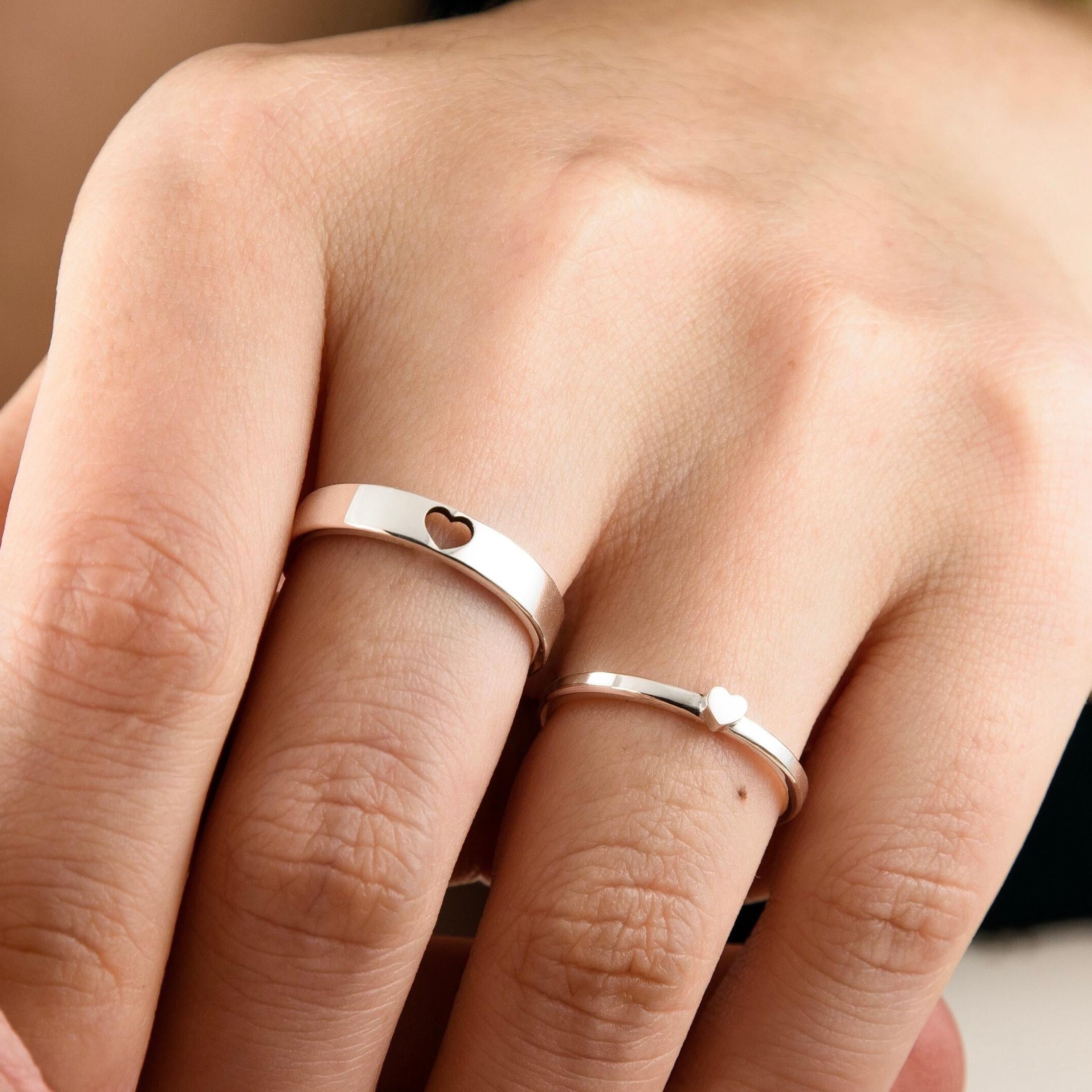 A matching set of sterling silver couple rings is shown on hand. The men’s ring features a cut-out heart, while the women’s band displays a solid heart that fits into the cut-out. Their minimalist style and interlocking design symbolize connection and affection. Crafted in 925 silver, these rings are ideal for daily wear and make a romantic promise gift with a customizable message inside.